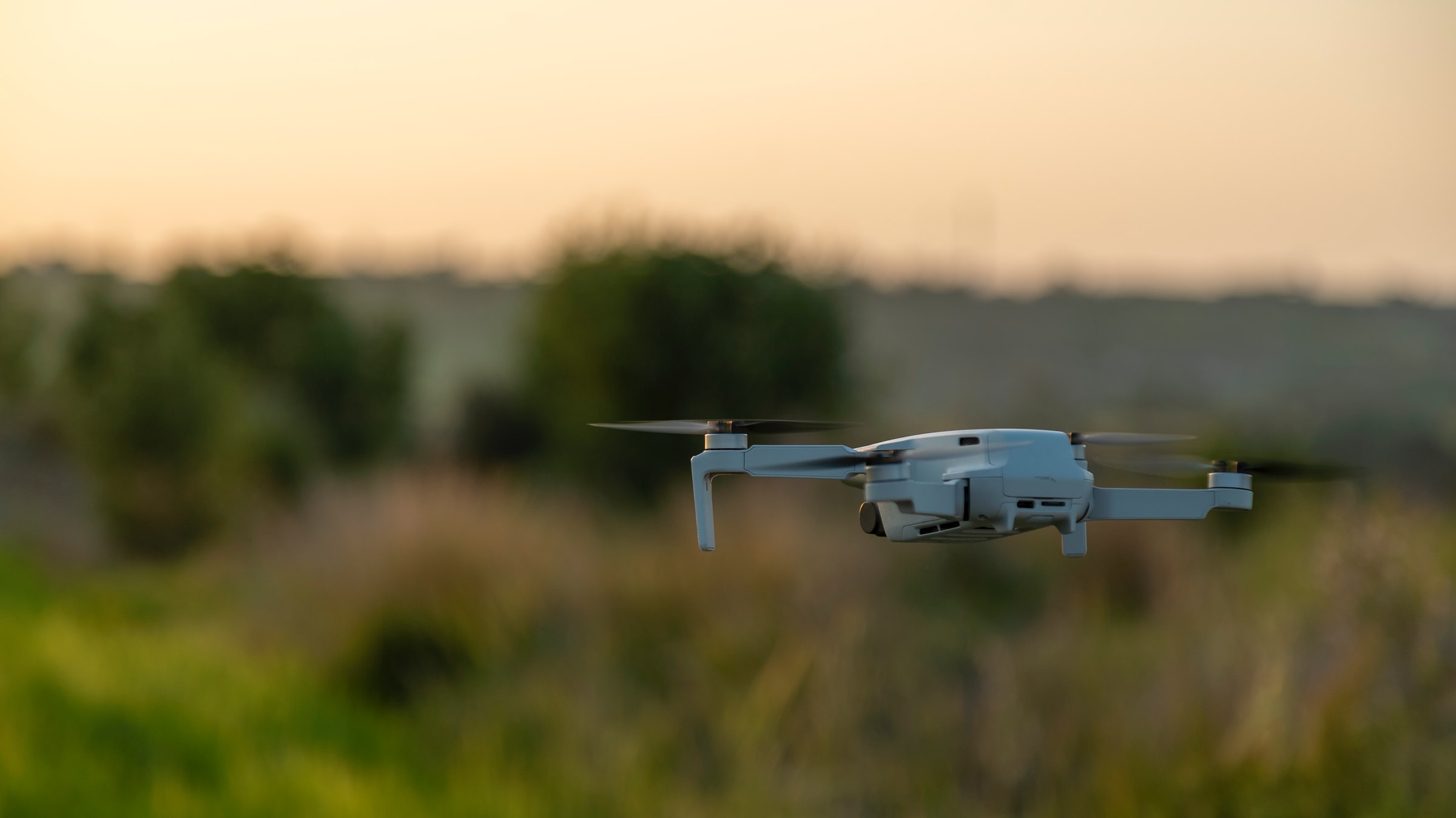 En drone hovrer over bakken, klar til å filme en eng i solnedgang.